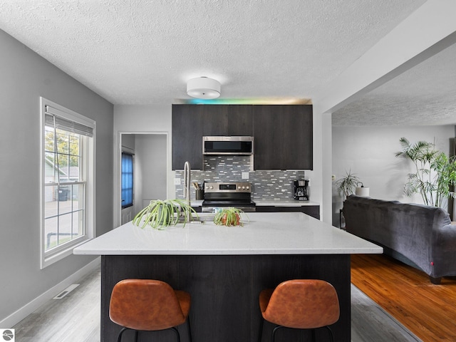 kitchen with appliances with stainless steel finishes, a textured ceiling, a kitchen breakfast bar, light wood finished floors, and modern cabinets
