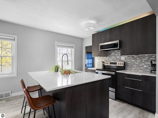 kitchen featuring stainless steel appliances, a sink, a breakfast bar area, tasteful backsplash, and light wood-style flooring