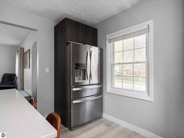 kitchen featuring stainless steel refrigerator with ice dispenser, a textured ceiling, light wood-style floors, light countertops, and baseboards