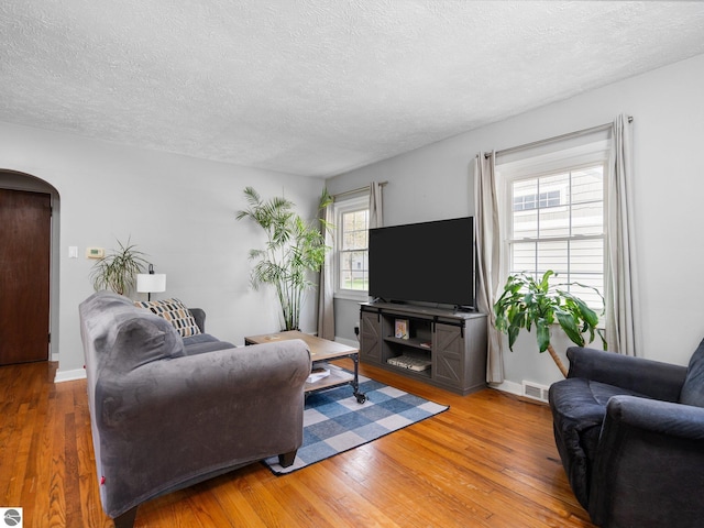 living room featuring arched walkways, wood-type flooring, a textured ceiling, and baseboards