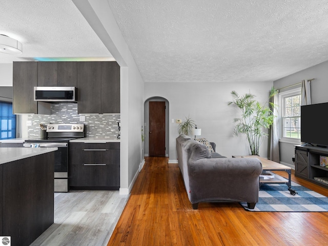 living area featuring arched walkways, a textured ceiling, light wood-type flooring, and baseboards