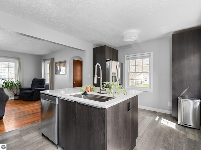 kitchen with stainless steel appliances, a sink, arched walkways, light countertops, and a textured ceiling
