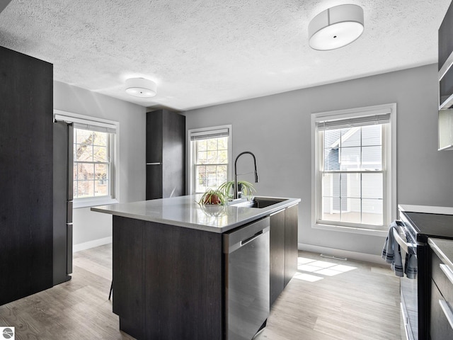 kitchen featuring stainless steel appliances, a sink, light wood-type flooring, baseboards, and an island with sink
