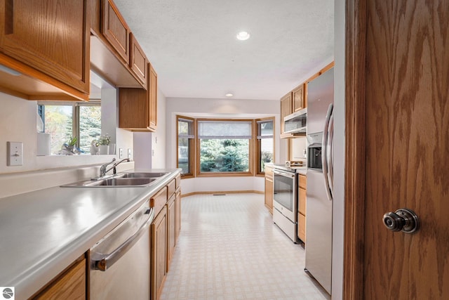 3691 Eastview Dr Unit 67, Traverse City, MI 49684 - kitchen featuring appliances with stainless steel finishes, a sink, brown cabinets, light floors, and plenty of natural light