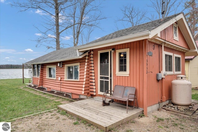 rear view of property featuring a lawn, log exterior, a water view, and a shingled roof