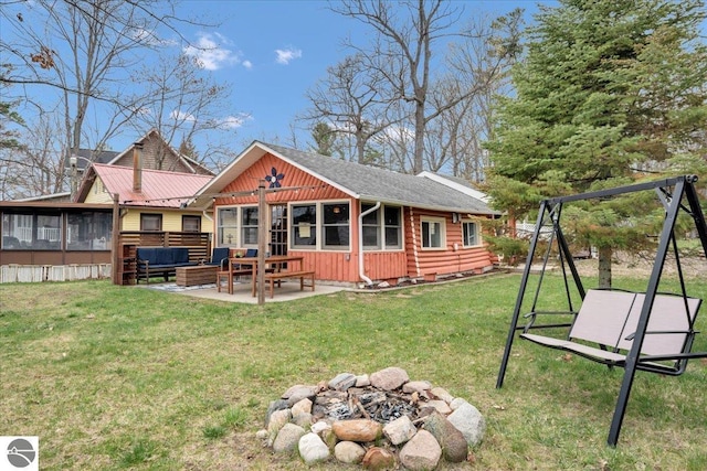 back of property with a sunroom, board and batten siding, a patio, an outdoor living space with a fire pit, and a yard