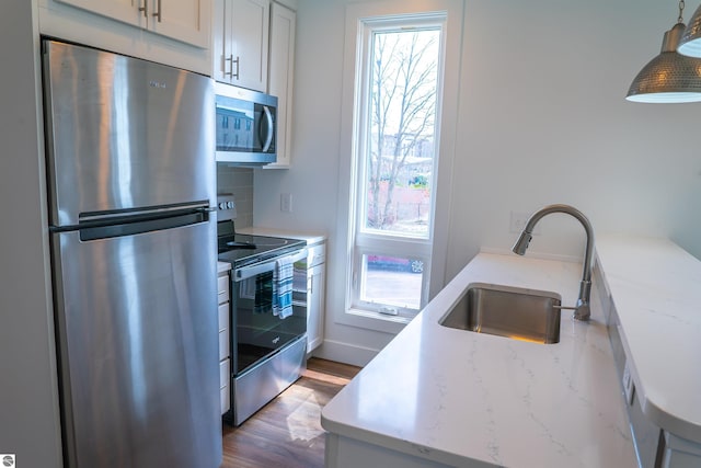 kitchen with stainless steel appliances, a sink, wood finished floors, tasteful backsplash, and light stone counters