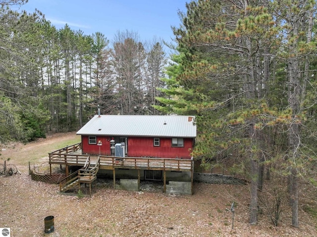 view of front facade featuring a wooden deck, a wooded view, and metal roof