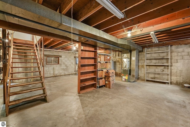 unfinished basement featuring stairway and heating unit