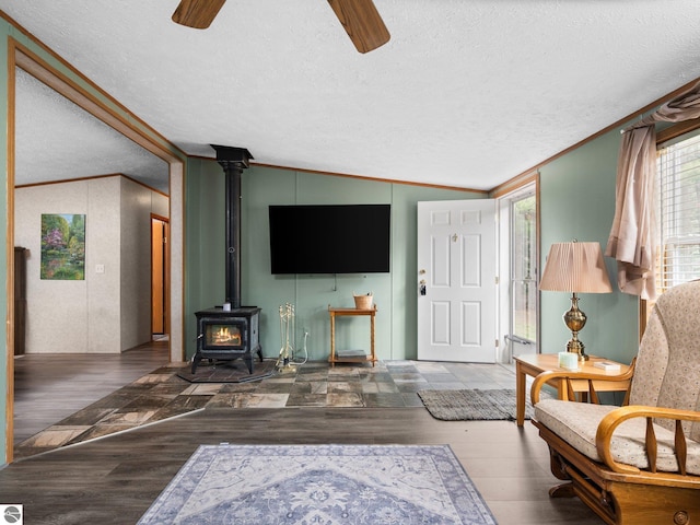 12036 SW Spring Creek Rd, Fife Lake, MI 49633 - living room featuring ceiling fan, ornamental molding, a wood stove, a textured ceiling, and wood finished floors