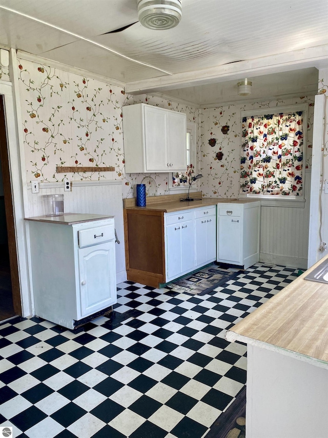kitchen featuring light floors, white cabinetry, wallpapered walls, light countertops, and a wainscoted wall