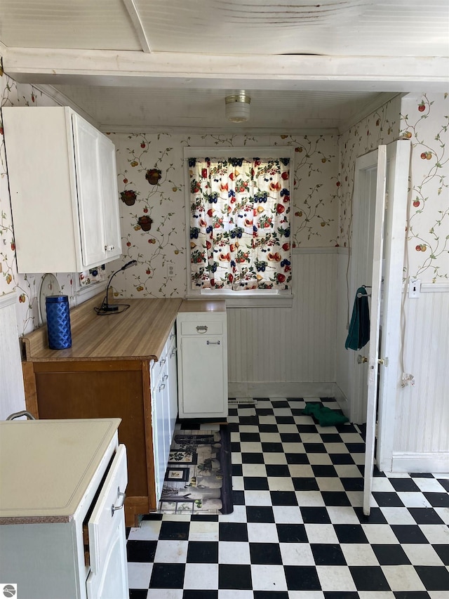 kitchen featuring light flooring, wainscoting, light countertops, white cabinets, and wallpapered walls