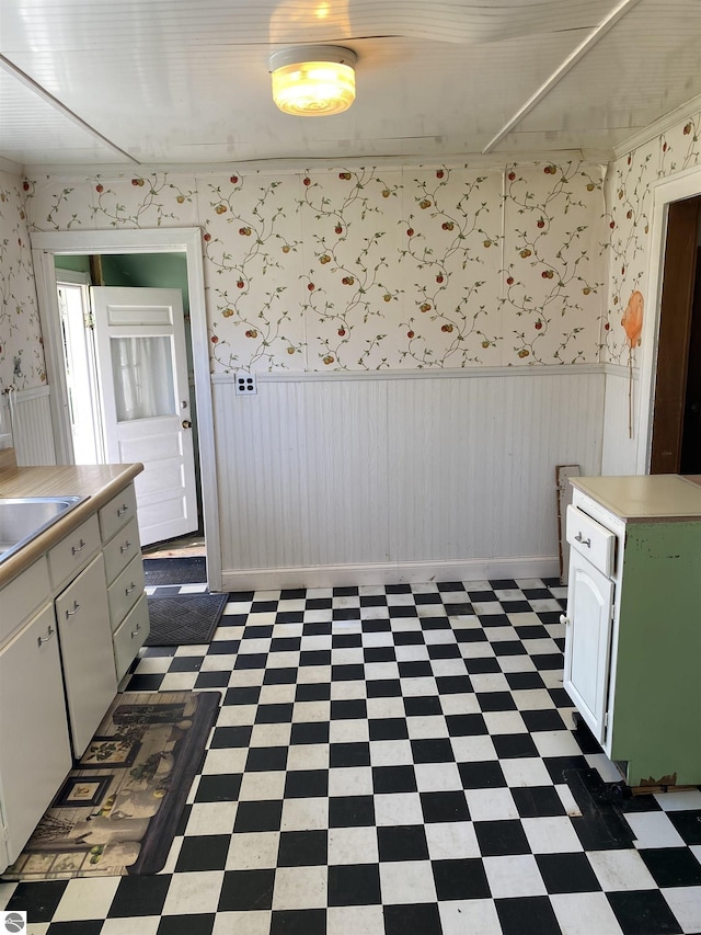 unfurnished dining area with tile patterned floors, wainscoting, a sink, and wallpapered walls