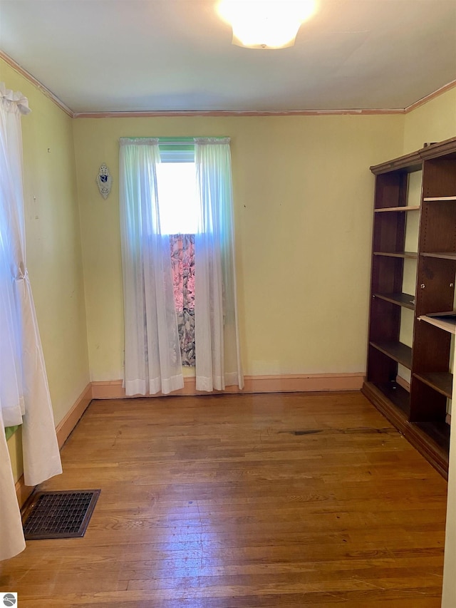 spare room with ornamental molding, wood-type flooring, and baseboards