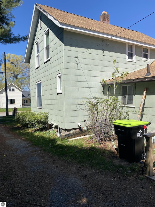 rear view of property featuring a chimney and a shingled roof