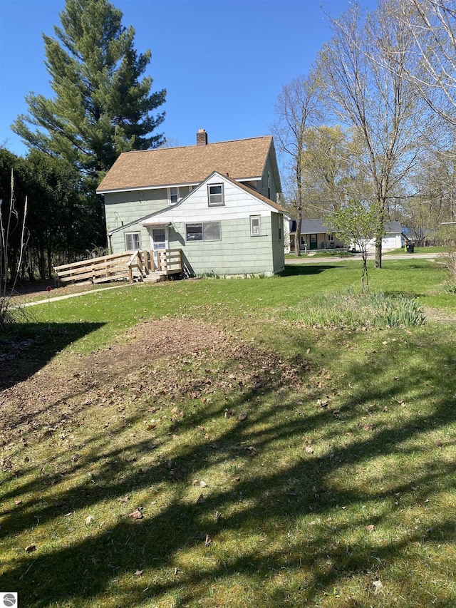 back of property with a chimney, a lawn, and roof with shingles