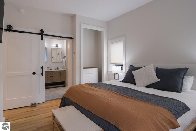 127 River St, Elk Rapids, MI 49629 - bedroom featuring light wood-type flooring, a barn door, and connected bathroom
