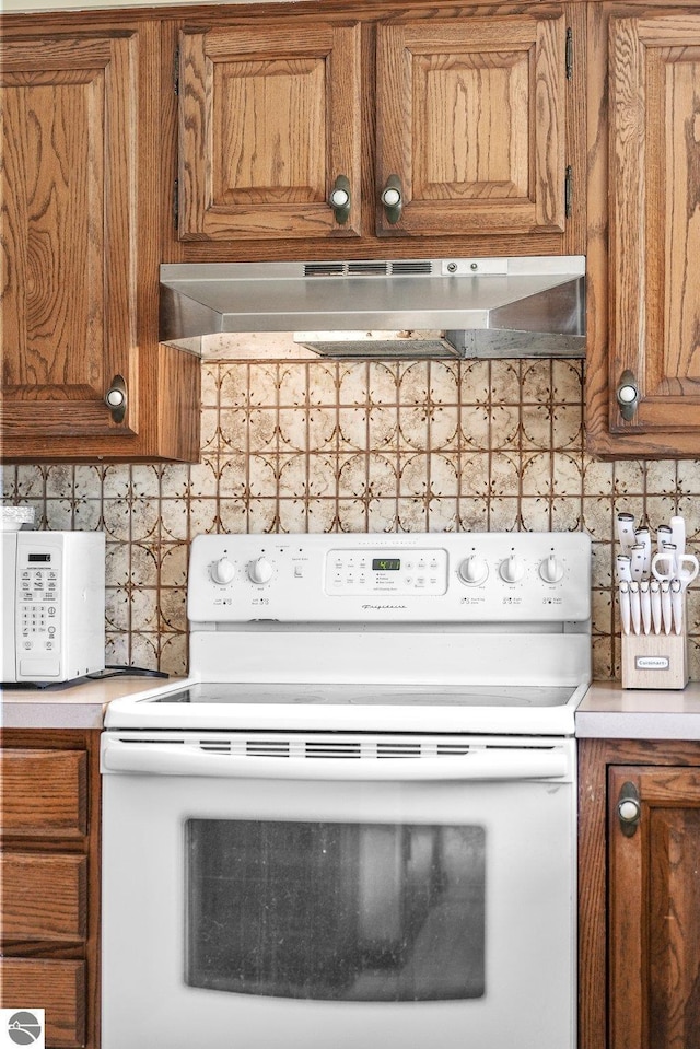 11531 S Tower Rd, Maple City, MI 49664 - kitchen view of white appliances, brown cabinetry, under cabinet range hood, backsplash, and light countertops