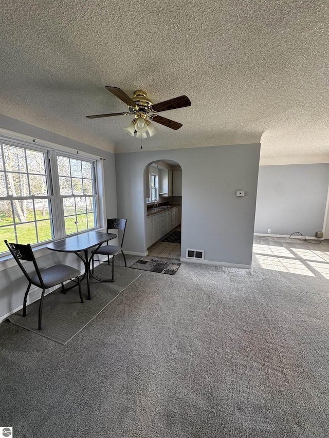 sitting room with arched walkways, carpet floors, a ceiling fan, baseboards, and a textured ceiling