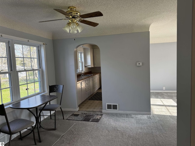 dining room featuring arched walkways, a textured ceiling, light carpet, ceiling fan, and baseboards