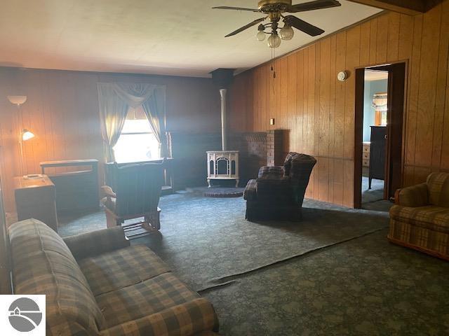 8067 Cherry Ave, Rapid City, MI 49676 - carpeted living area featuring a wood stove, wood walls, and a ceiling fan
