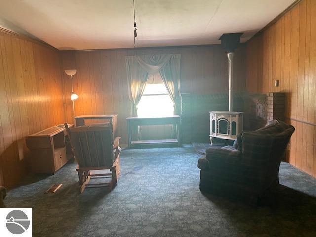 8067 Cherry Ave, Rapid City, MI 49676 - sitting room featuring wood walls, a wood stove, carpet flooring, and a fireplace