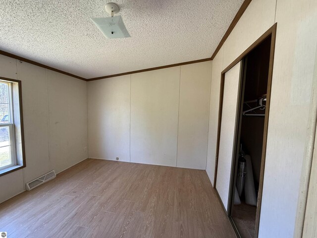 3072 Gonder Rd, Interlochen, MI 49643 - unfurnished bedroom featuring crown molding, wood finished floors, a textured ceiling, and a decorative wall