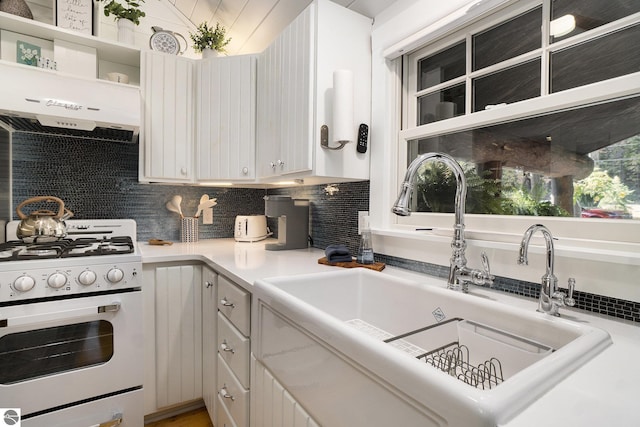 421 S Shabwasung St, Northport, MI 49670 - kitchen with white gas stove, a sink, decorative backsplash, light countertops, and white cabinetry