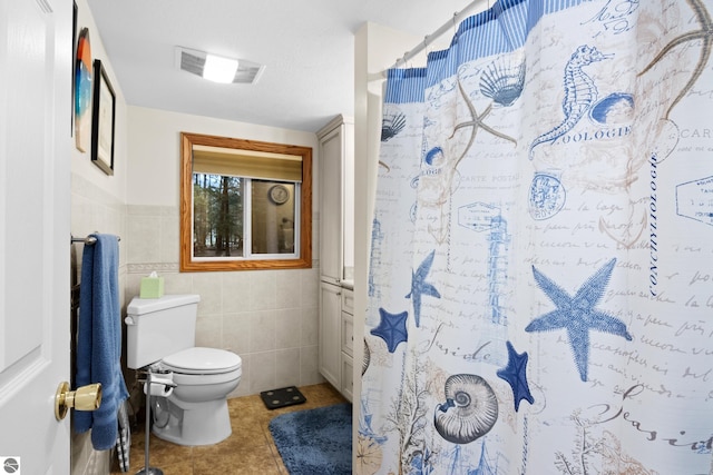 bathroom featuring tile walls, tile patterned floors, toilet, a shower with curtain, and a wainscoted wall