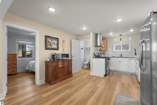 1750 S Schneider St, Lake City, MI 49651 - kitchen featuring appliances with stainless steel finishes, wall chimney exhaust hood, light wood-type flooring, a sink, and white cabinets