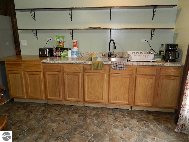kitchen featuring a sink, dark stone finish floors, light countertops, and brown cabinets