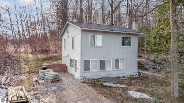 view of home's exterior with a chimney, roof with shingles, and view of wooded area