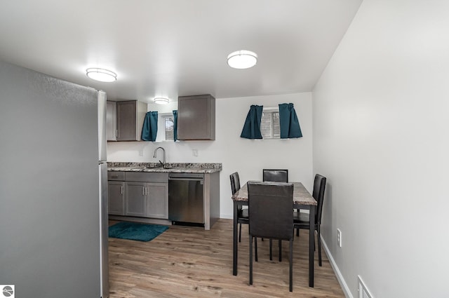 kitchen with appliances with stainless steel finishes, light wood finished floors, a sink, and baseboards
