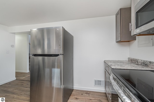 kitchen featuring stainless steel appliances, light wood-style flooring, baseboards, light countertops, and dark brown cabinets