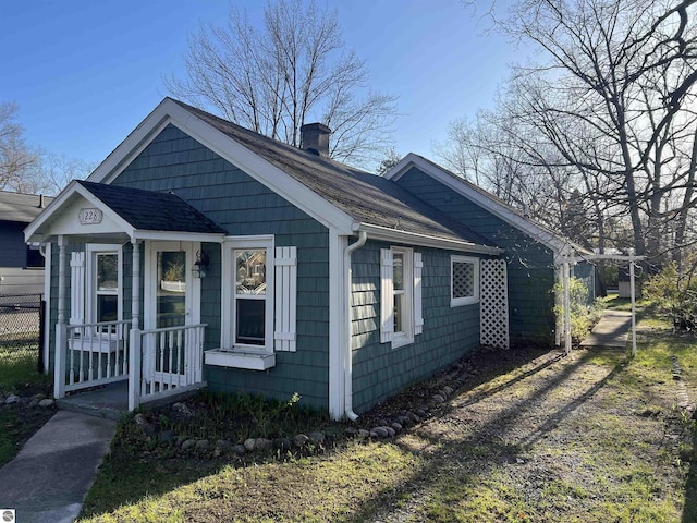 view of front facade featuring a shingled roof, a chimney, and fence