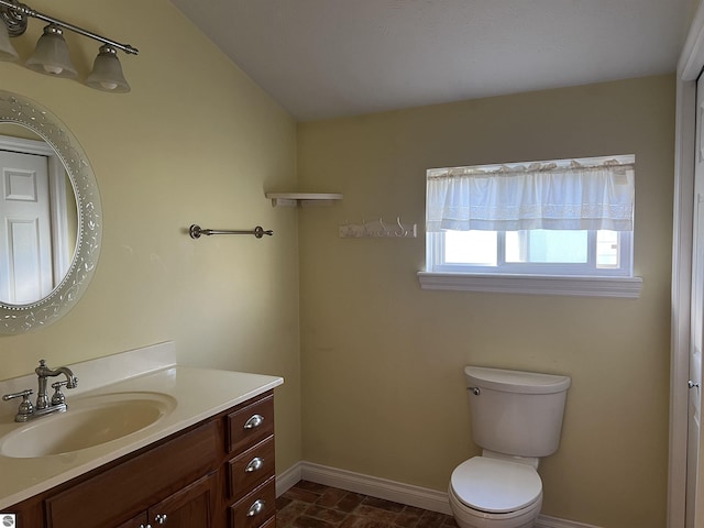 bathroom with baseboards, toilet, vanity, and stone finish flooring