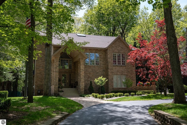 view of front of house with brick siding, a front yard, and a shingled roof