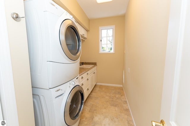 washroom with stacked washer / drying machine, cabinet space, baseboards, and stone finish flooring