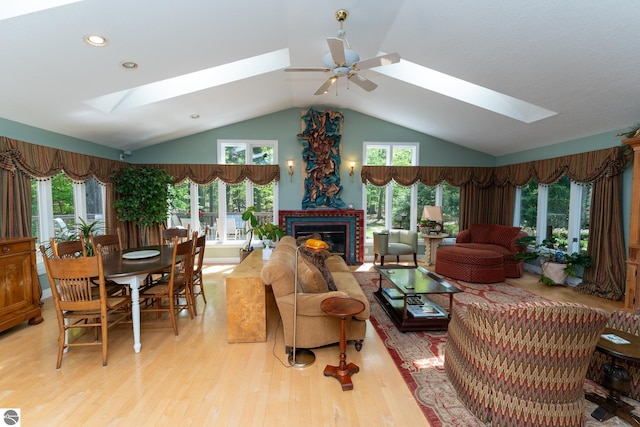living room featuring a skylight, ceiling fan, vaulted ceiling, light wood finished floors, and a brick fireplace