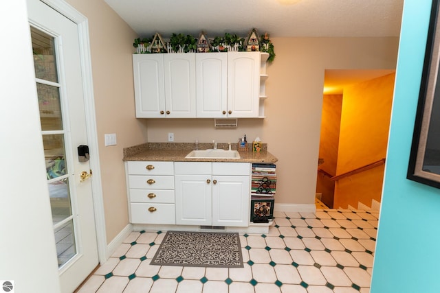 kitchen featuring a sink, white cabinetry, light floors, and baseboards
