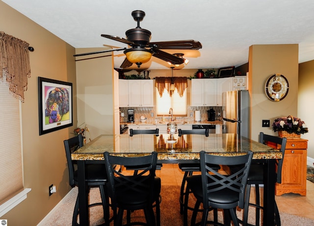 11255 E Fort Rd Unit H1, Suttons Bay, MI 49682 - kitchen featuring freestanding refrigerator, a ceiling fan, a kitchen breakfast bar, white cabinetry, and decorative backsplash