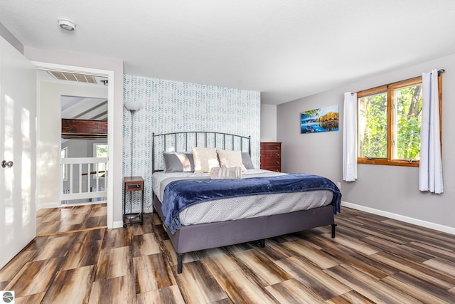 5540 Golf Meadows Dr, Bellaire, MI 49615 - bedroom featuring wallpapered walls, an accent wall, wood finished floors, and baseboards