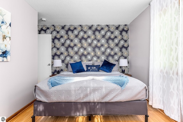 5540 Golf Meadows Dr, Bellaire, MI 49615 - bedroom featuring an accent wall, wallpapered walls, wood finished floors, and baseboards