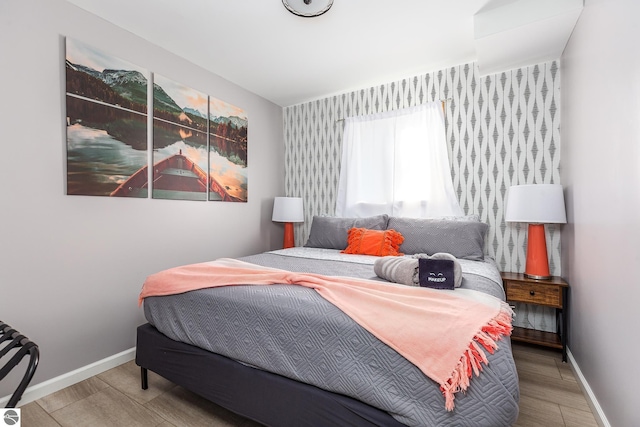 5540 Golf Meadows Dr, Bellaire, MI 49615 - bedroom featuring wallpapered walls, baseboards, wood finished floors, and an accent wall