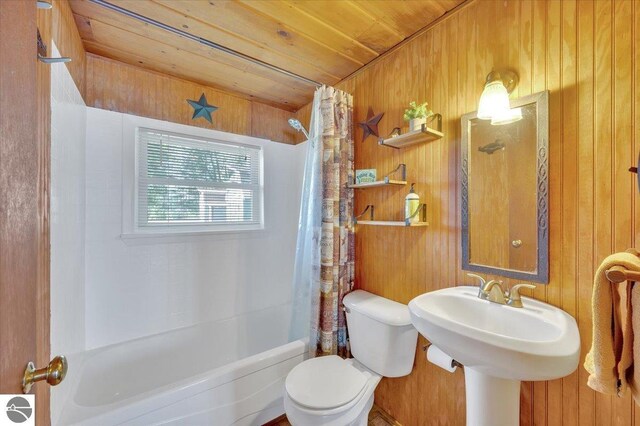 full bathroom with wooden ceiling, toilet, wooden walls, shower / bathtub combination with curtain, and a sink