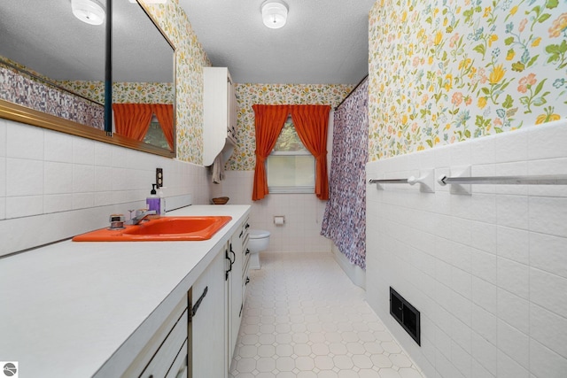 7548 S Dune Hwy, Empire, MI 49630 - bathroom featuring wallpapered walls, tile walls, toilet, vanity, and tile patterned flooring