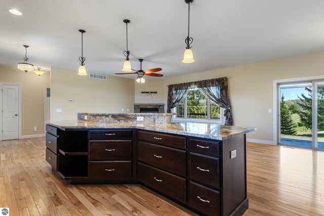 8233 Barney Rd, Traverse City, MI 49684 - kitchen with a ceiling fan, light wood-style flooring, baseboards, a stone fireplace, and dark brown cabinetry