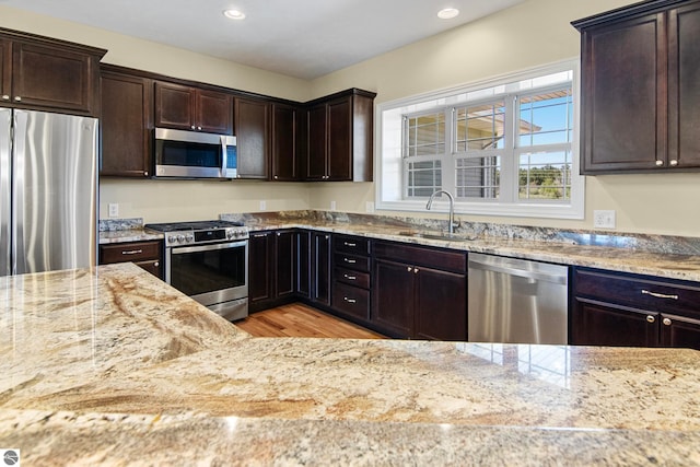 8233 Barney Rd, Traverse City, MI 49684 - kitchen with appliances with stainless steel finishes, a sink, light stone countertops, light wood-style flooring, and recessed lighting