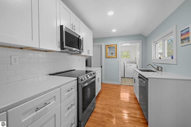 kitchen featuring appliances with stainless steel finishes, washing machine and dryer, a sink, light countertops, and tasteful backsplash