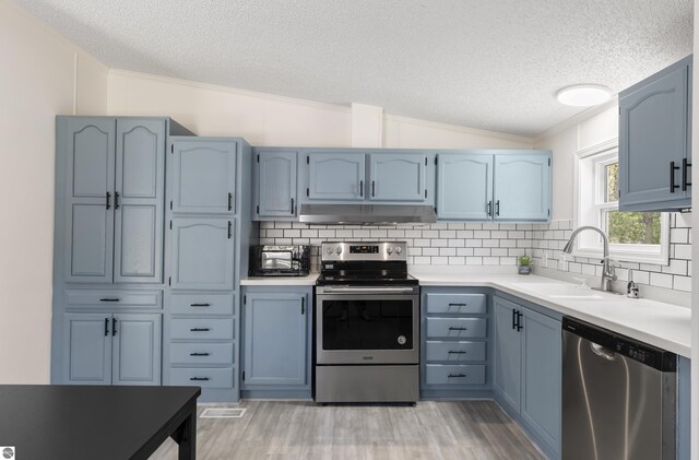 kitchen featuring stainless steel appliances, a sink, under cabinet range hood, lofted ceiling, and a textured ceiling